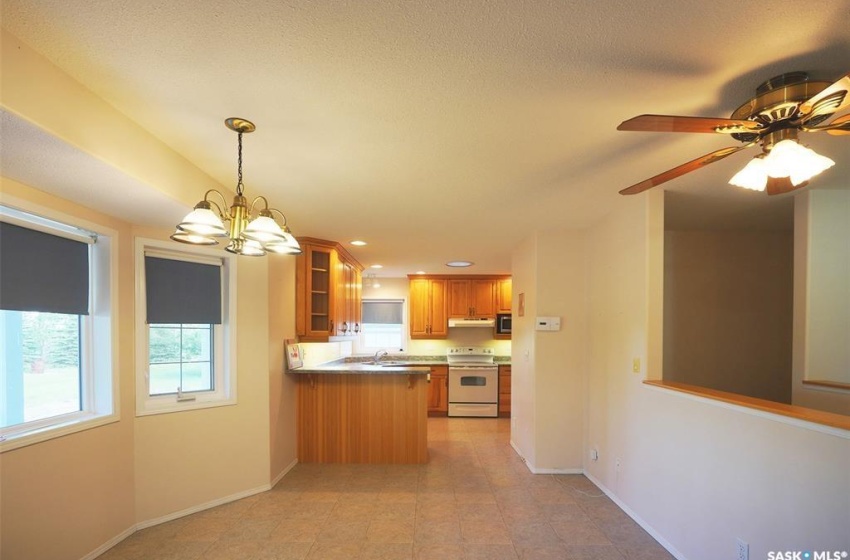 Kitchen with light tile floors, white electric range, ceiling fan with notable chandelier, kitchen peninsula, and pendant lighting