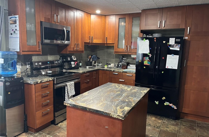 Kitchen featuring range with electric cooktop, a kitchen island, tasteful backsplash, black refrigerator, and dark stone counters