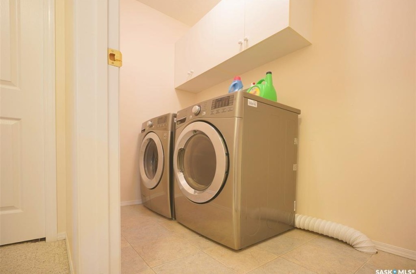 Washroom with independent washer and dryer, light tile floors, and cabinets