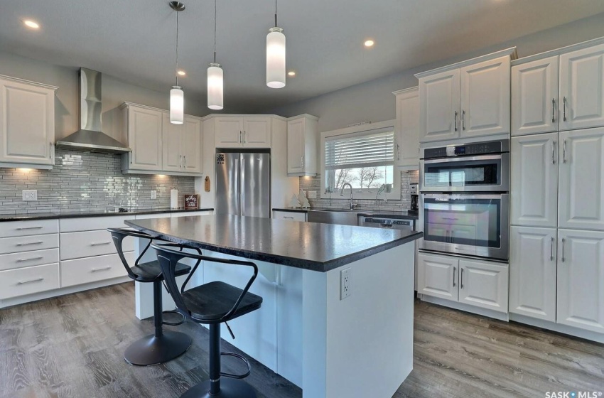 Kitchen featuring wall chimney range hood, light hardwood / wood-style floors, white cabinetry, and appliances with stainless steel finishes