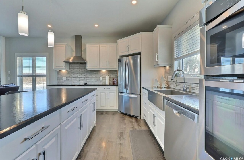 Kitchen with wall chimney exhaust hood, pendant lighting, stainless steel appliances, tasteful backsplash, and white cabinets