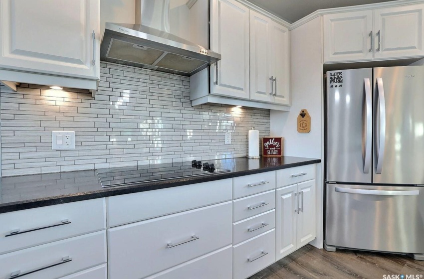 Kitchen with dark hardwood / wood-style floors, stainless steel fridge, wall chimney range hood, and white cabinetry