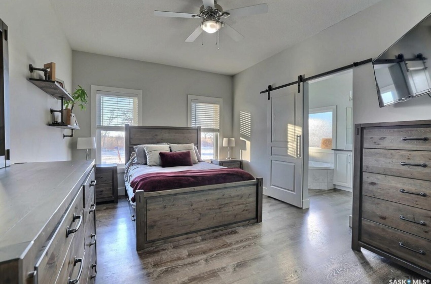 Bedroom featuring a barn door, ceiling fan, light wood-type flooring, and ensuite bath