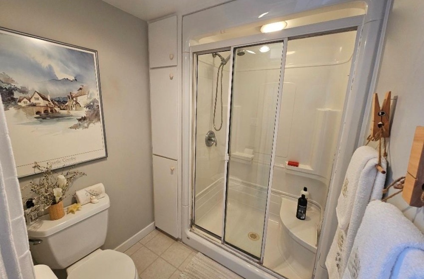 Bathroom featuring toilet, a shower with door, and tile flooring