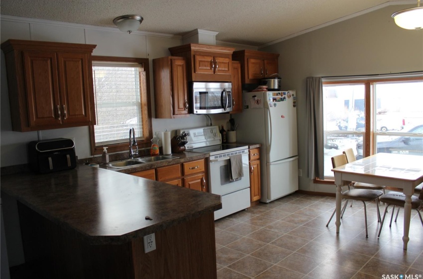 Kitchen featuring sink, crown molding, vaulted ceiling, dark tile flooring, and white appliances