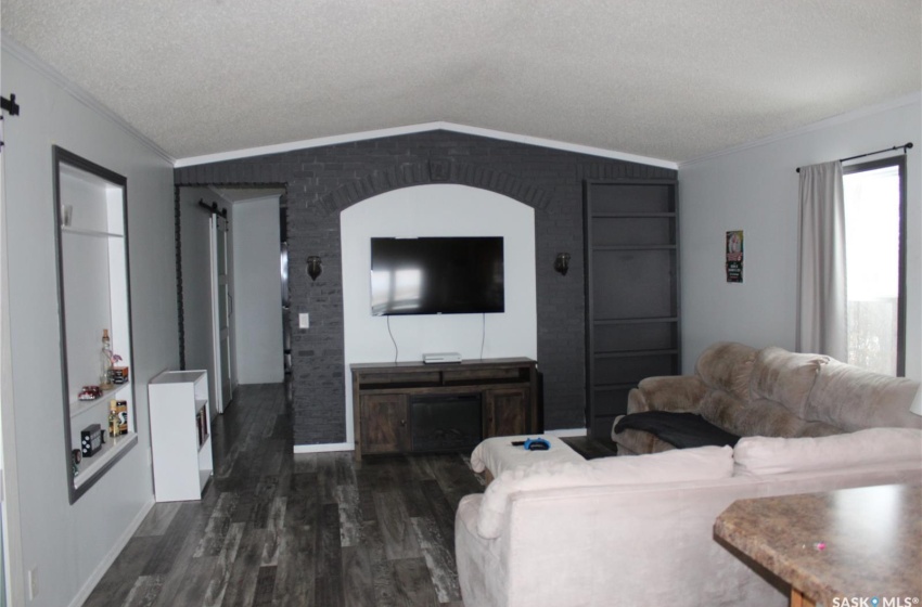 Living room with dark wood-type flooring, a textured ceiling, ornamental molding, and vaulted ceiling