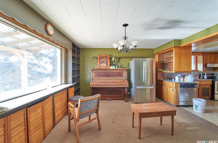 Kitchen featuring light carpet, a chandelier, hanging light fixtures, appliances with stainless steel finishes, and exhaust hood