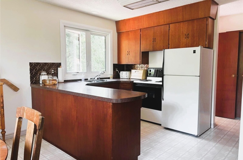 Kitchen featuring kitchen peninsula, white appliances, light floors, sink, and tasteful backsplash