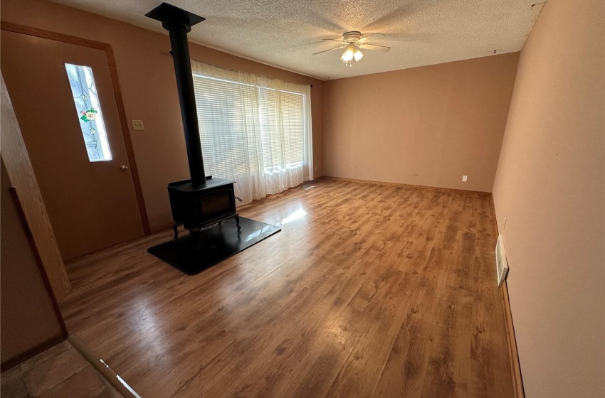 Unfurnished living room featuring light hardwood / wood-style floors, a wood heater, a textured ceiling, and ceiling fan