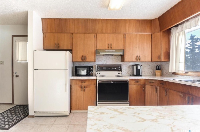 Kitchen featuring light tile flooring, a textured ceiling, white appliances, and backsplash