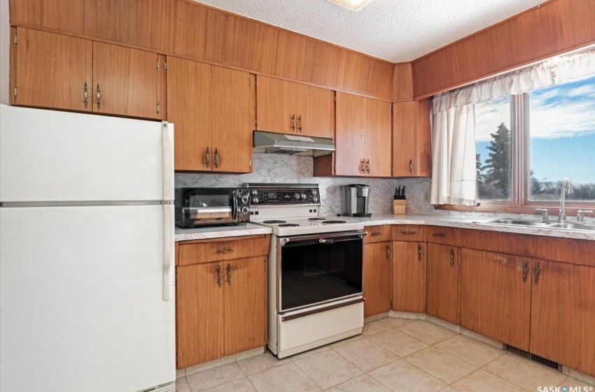 Kitchen with white appliances, a textured ceiling, light tile floors, sink, and tasteful backsplash