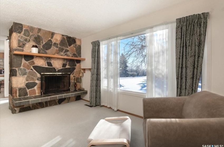 Carpeted living room with plenty of natural light, a stone fireplace, and a textured ceiling