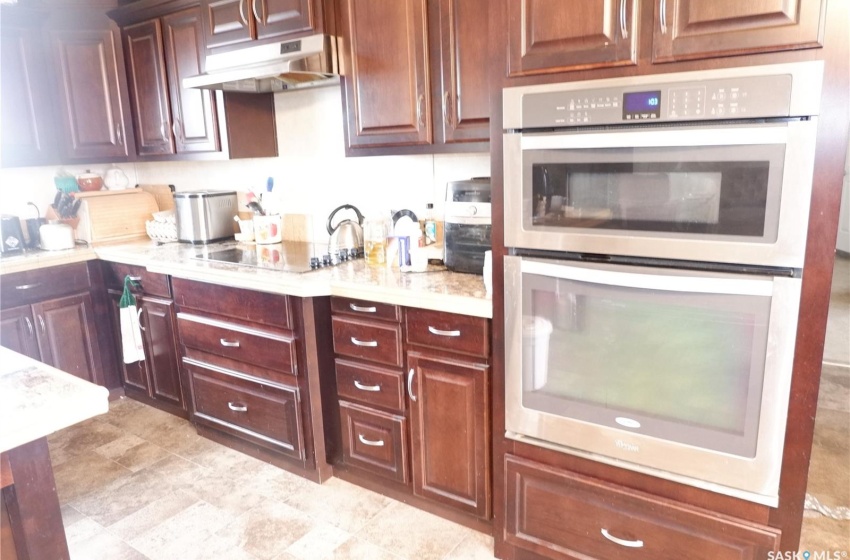 Kitchen with black electric stovetop, double oven, light stone counters, and light tile flooring