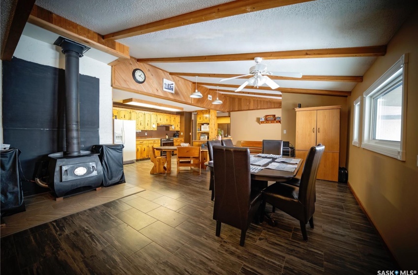 Dining space featuring a textured ceiling, lofted ceiling with beams, ceiling fan, a wood stove, and dark hardwood / wood-style flooring