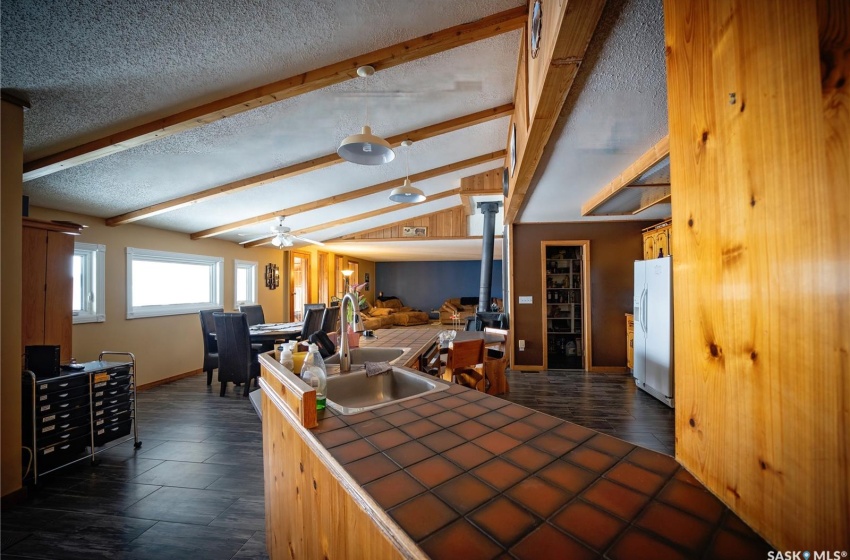 Kitchen featuring tile counters, lofted ceiling with beams, a textured ceiling, white refrigerator with ice dispenser, and ceiling fan