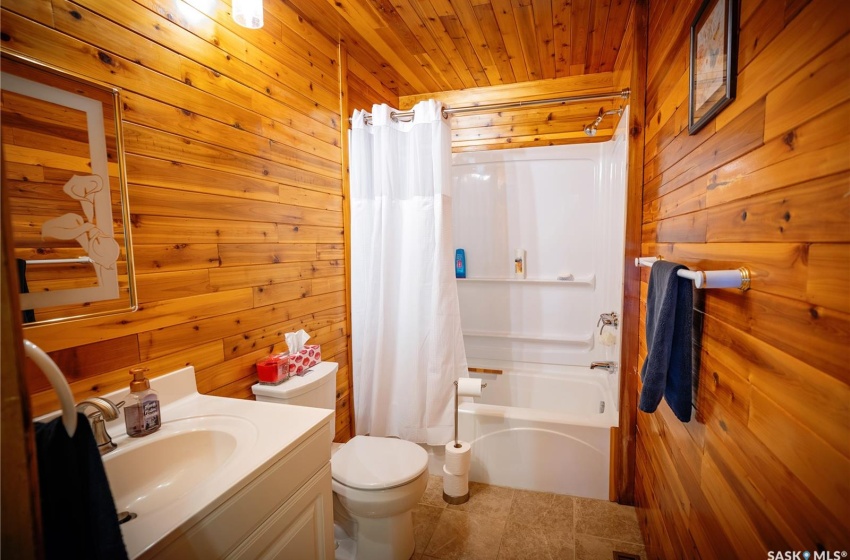 Full bathroom with toilet, wooden ceiling, shower / bath combo with shower curtain, and wood walls