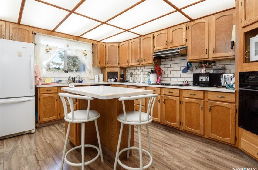 Kitchen with light hardwood / wood-style flooring, white appliances, range hood, and backsplash