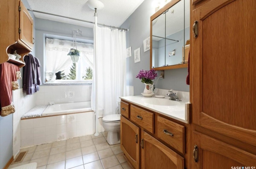 Bathroom featuring tile flooring, toilet, a textured ceiling, a relaxing tiled bath, and oversized vanity