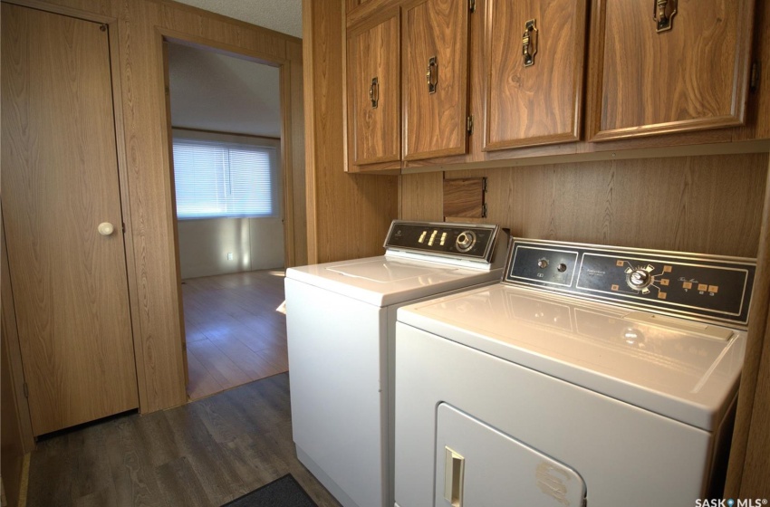 Laundry room with dark wood-type flooring, wooden walls, cabinets, and independent washer and dryer