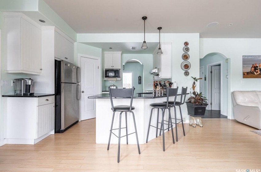 Kitchen featuring stainless steel refrigerator, hanging light fixtures, light hardwood / wood-style flooring, a kitchen breakfast bar, and black microwave