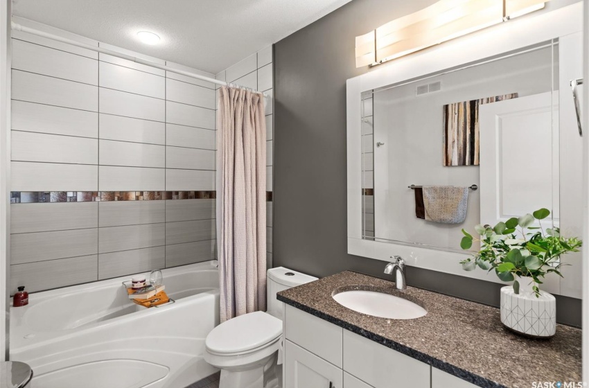 Full bathroom with large vanity, shower / bath combo with shower curtain, and toilet