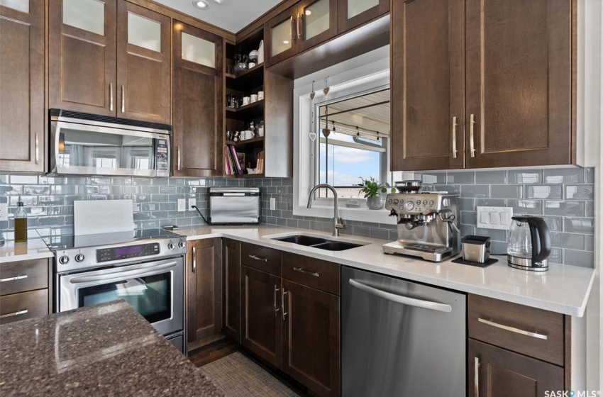 Kitchen featuring dark brown cabinets, tasteful backsplash, sink, dark stone countertops, and appliances with stainless steel finishes