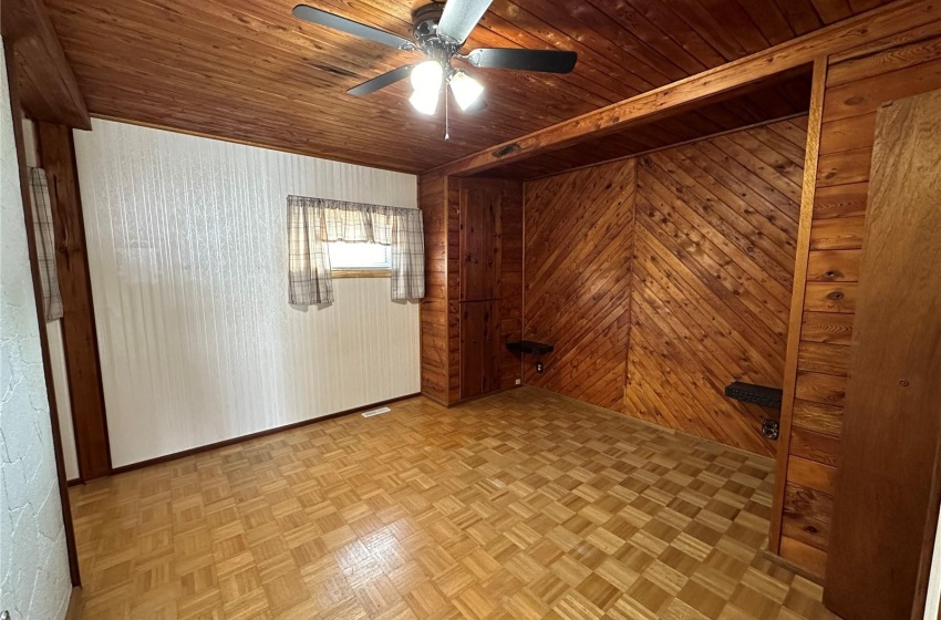 Empty room with wood ceiling, wooden walls, ceiling fan, and light parquet floors