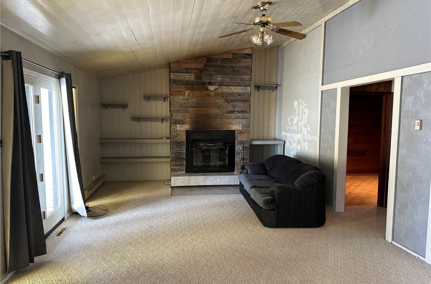 Living room with a stone fireplace, light colored carpet, lofted ceiling, wooden walls, and ceiling fan