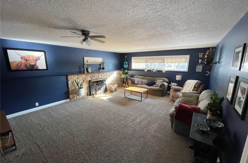 Living room featuring a stone fireplace, ceiling fan, a textured ceiling, and carpet