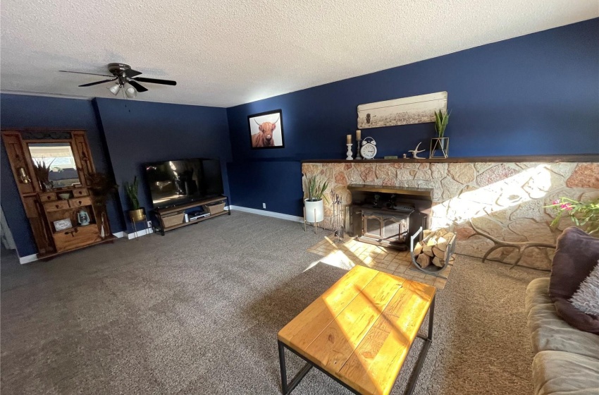 Unfurnished living room with a fireplace, dark colored carpet, ceiling fan, and a textured ceiling