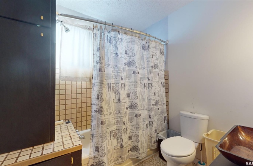 Bathroom with shower / bath combination with curtain, a textured ceiling, and toilet