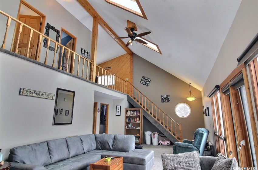 Living room with ceiling fan, high vaulted ceiling, beam ceiling, a skylight, and carpet floors