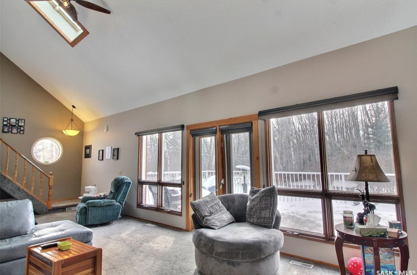 Carpeted living room featuring high vaulted ceiling, a skylight, and ceiling fan