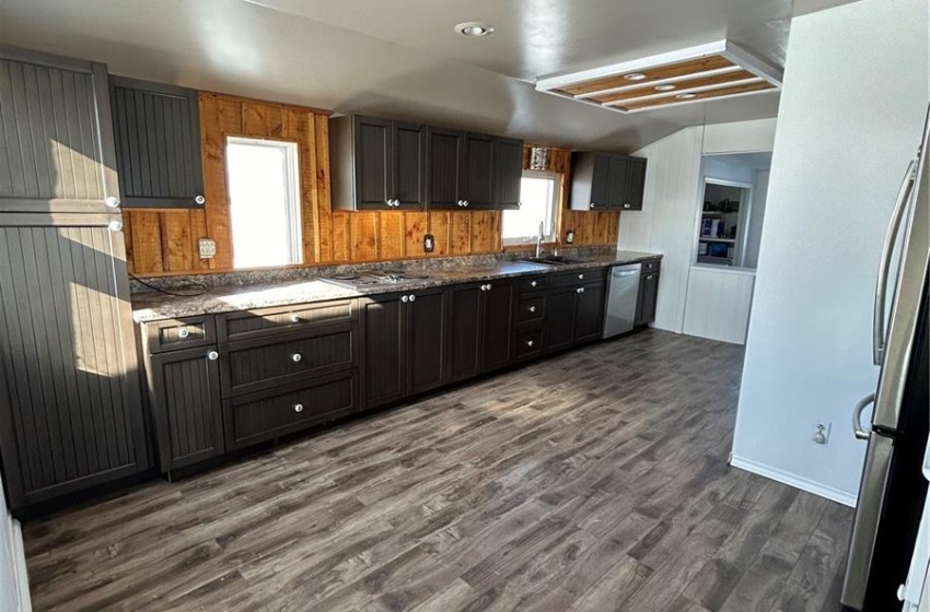 Kitchen featuring stainless steel dishwasher, sink, dark stone countertops, and hardwood / wood-style flooring