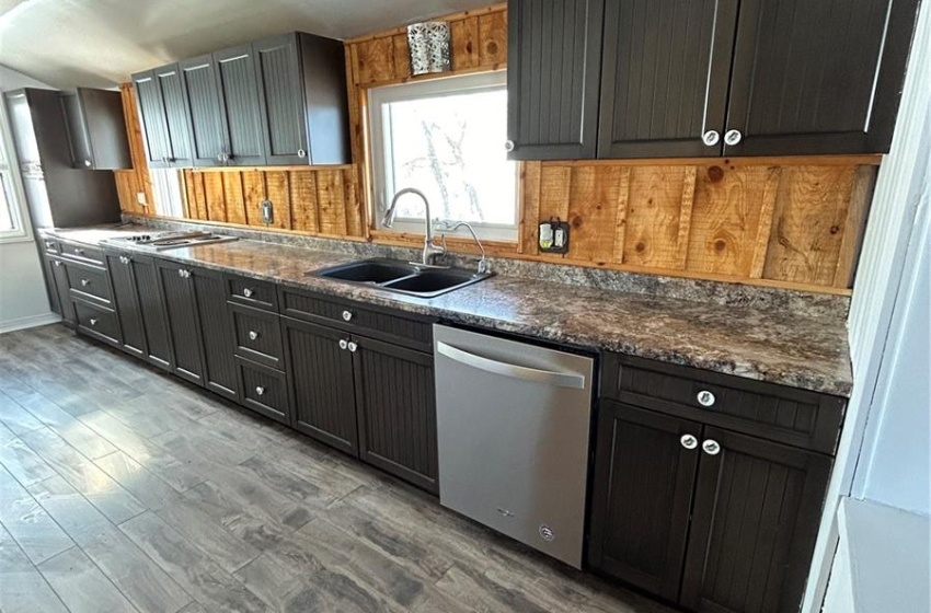 Kitchen featuring stainless steel dishwasher, sink, dark stone countertops, and hardwood / wood-style flooring