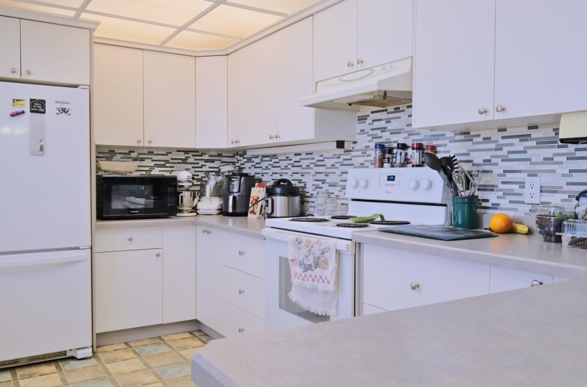 Kitchen featuring tasteful backsplash, white appliances, light tile floors, and white cabinets