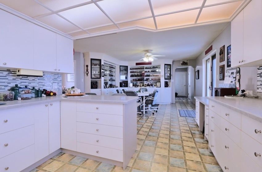 Kitchen featuring backsplash, white cabinets, light tile flooring, kitchen peninsula, and ceiling fan