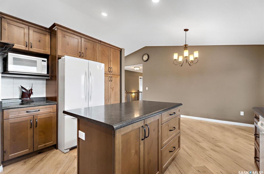 Kitchen featuring a center island, white appliances, light wood-type flooring, lofted ceiling, and decorative light fixtures