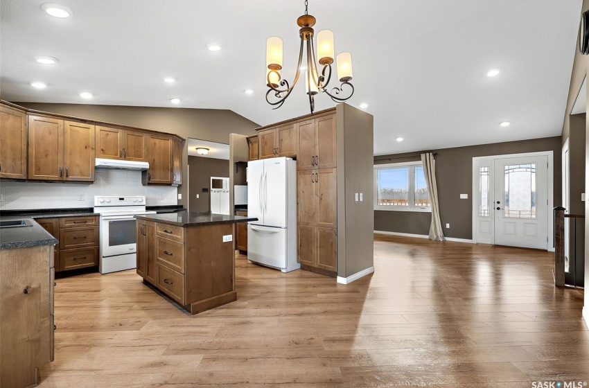 Kitchen with vaulted ceiling, pendant lighting, light hardwood / wood-style floors, white appliances, and a notable chandelier