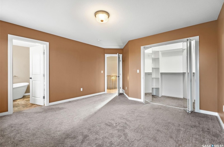 Unfurnished bedroom featuring a spacious closet, light carpet, ensuite bath, and a closet