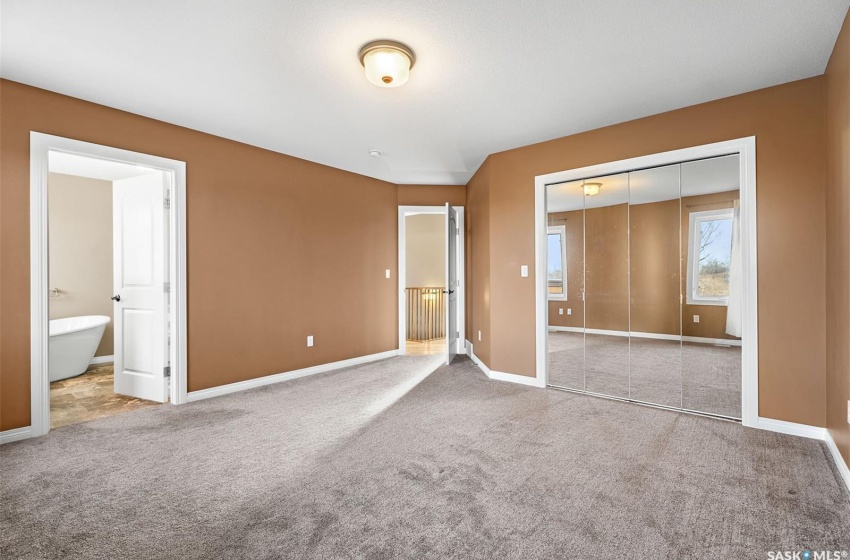 Unfurnished bedroom featuring light colored carpet, a closet, and ensuite bath