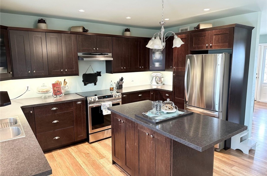 Kitchen with light hardwood / wood-style flooring, a kitchen island, hanging light fixtures, dark brown cabinets, and appliances with stainless steel finishes