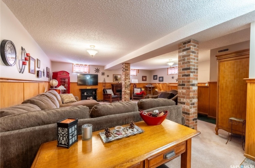 Living room with light colored carpet, a textured ceiling, brick wall, and ornate columns