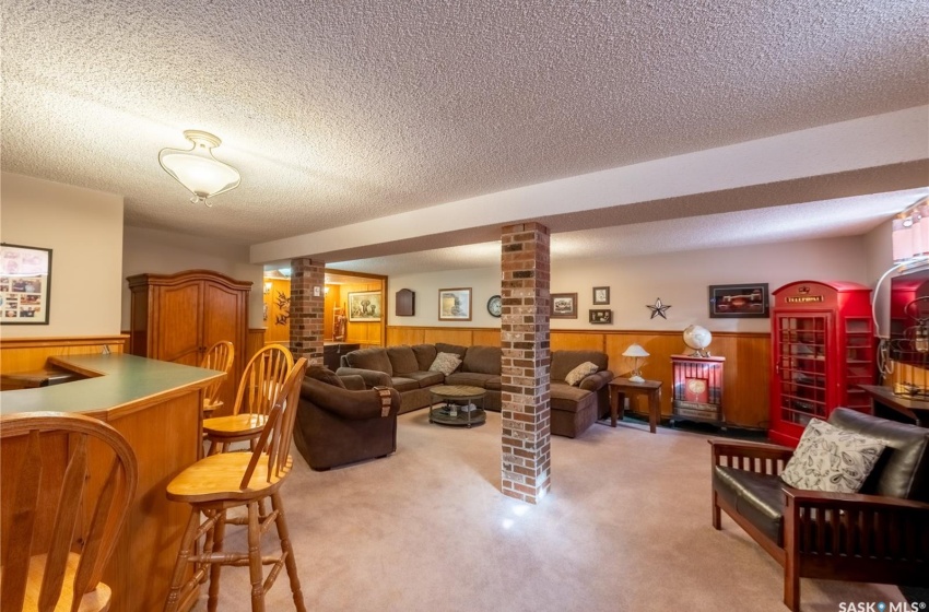 Living room featuring light carpet, a textured ceiling, decorative columns, and brick wall