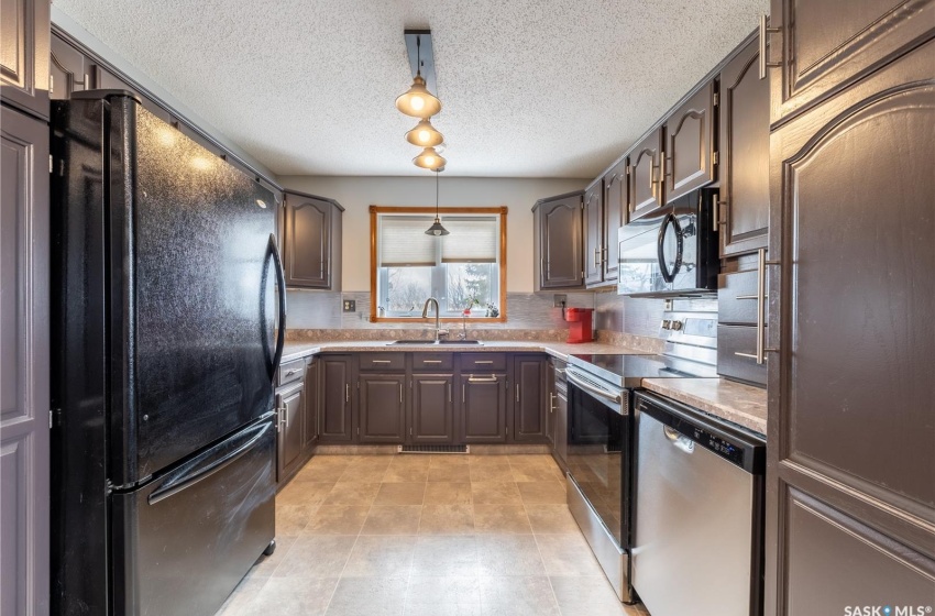 Kitchen featuring light tile flooring, black appliances, sink, a textured ceiling, and pendant lighting