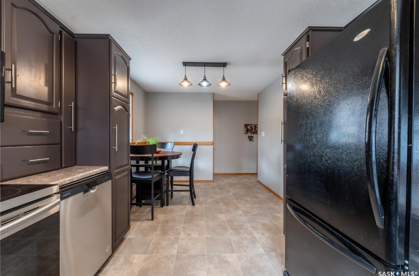 Kitchen featuring rail lighting, decorative light fixtures, light tile floors, dishwasher, and black fridge