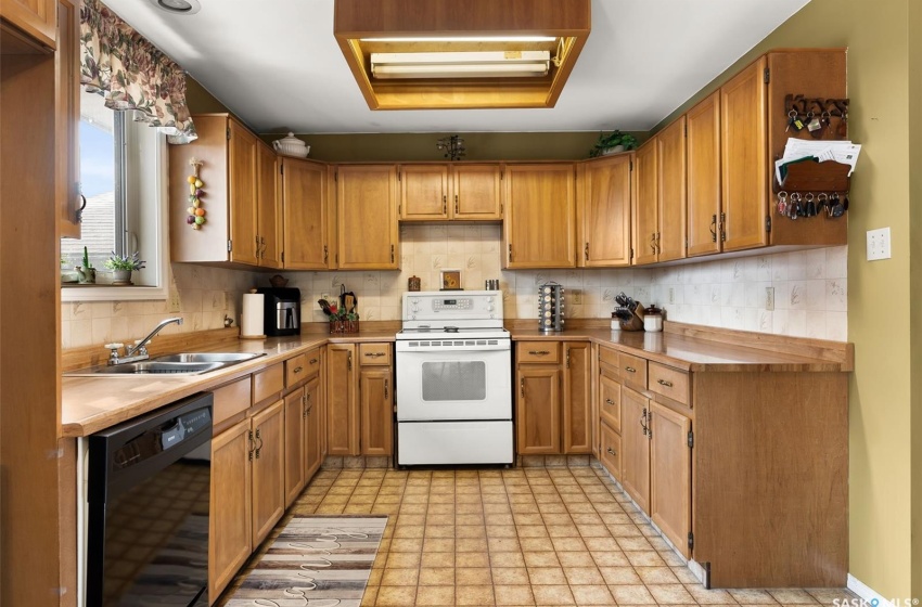 Kitchen with electric range, light tile flooring, sink, tasteful backsplash, and black dishwasher