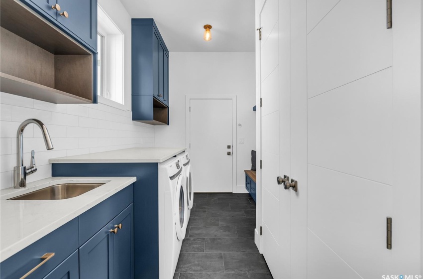 Laundry room with dark tile flooring, tasteful backsplash, sink, and dark blue cabinetry