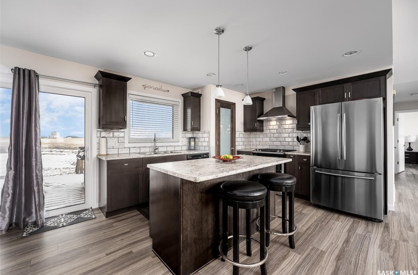 Kitchen with pendant lighting, tasteful backsplash, wall chimney exhaust hood, a center island, and stainless steel refrigerator