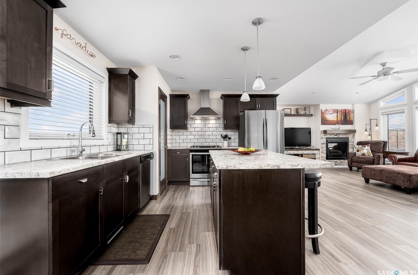 Kitchen featuring pendant lighting, a breakfast bar area, stainless steel appliances, wall chimney range hood, and a stone fireplace